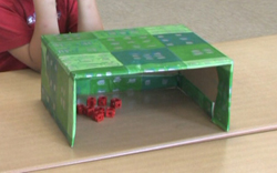 Foto einer Schachtel, die an einer Seite offen ist. Darunter liegen rote Steckwürfel.